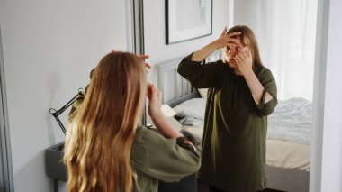 long-haired woman standing in front of a huge mirror in her bedroom and putting in contact lenses. High quality photo