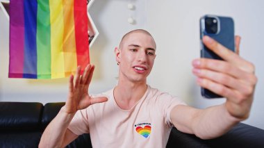 young Caucasian gay man talking in a live video, LGBT flag hanging on the shelves, LGBT concept. High quality photo