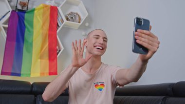 Young gay man taking selfie with LGBT flag in the background at home. High quality photo