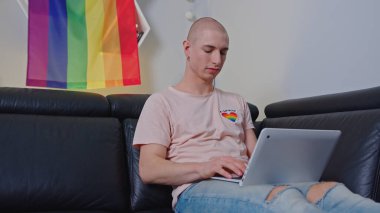 Queer non binary man using laptop with LGBT flag in the background. High quality photo
