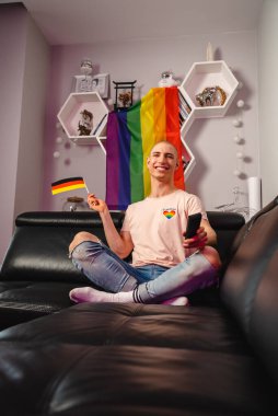 Smiling gay man waving Germany flag while watching TV. High quality photo