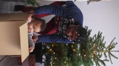 Alrican American father pushing his toddler son in a cardboard box on the floor on Christmas. High quality 4k footage