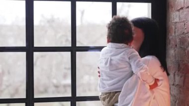 A young woman holding her toddler son, pointing through the window. High quality 4k footage