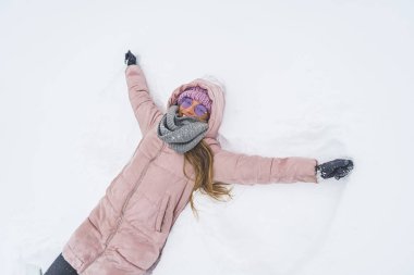 Overhead view of smiling woman lying on snow and making snow angel wings with hands . High quality photo