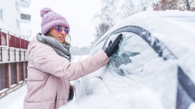 Woman removing the snow with her gloved hand off the car window . High quality photo