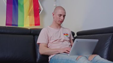 medium shot of a gay bald man on a sofa using his laptop, LGBT theme. High quality 4k footage