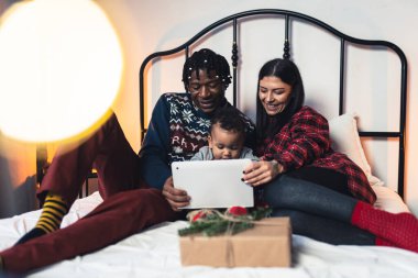 Anne ve baba, küçük tatlı bir Afro-Amerikalı çocuğa Noel hediyesini tabletle çekmesi için yardım ediyor. Yüksek kalite fotoğraf