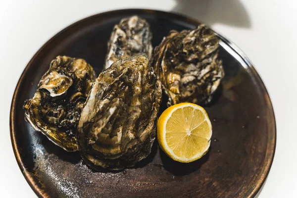 牡蠣はブラックプレートの上にオランダとレモンを形成し 独特の料理を作ります 高品質の写真 ストック画像