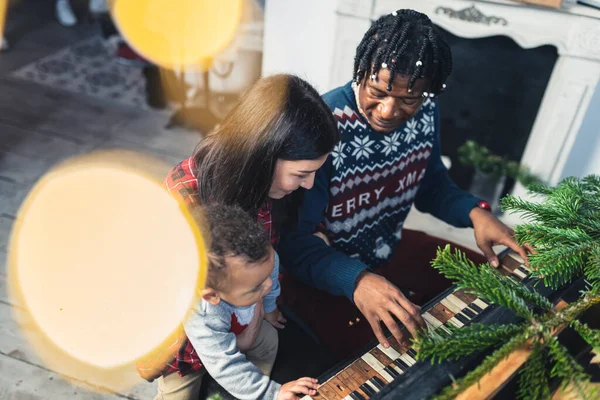 Afro-American man playing on the piano and his beloved Caucasian wife and a son watching him. High quality photo