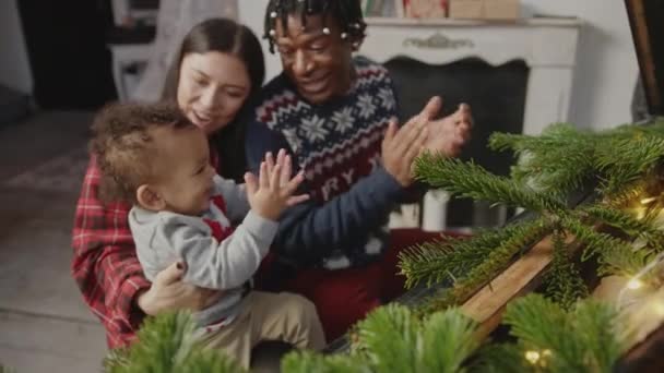 幸せな多人種のカップル彼らのかわいい息子と拍手 中ショットでクリスマスツリーを置く 高品質4K映像 — ストック動画