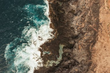 Güzel drone dalgaları günbatımında kayalarla yavaşça kıyıya vuruyor, yukarıdan inanılmaz mavi renkte.
