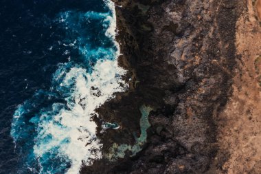 Güzel drone dalgaları günbatımında kayalarla yavaşça kıyıya vuruyor, yukarıdan inanılmaz mavi renkte.