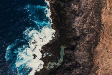 Güzel drone dalgaları günbatımında kayalarla yavaşça kıyıya vuruyor, yukarıdan inanılmaz mavi renkte.