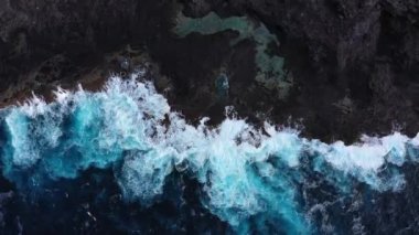 Güzel drone dalgaları günbatımında kayalarla yavaşça kıyıya vuruyor, yukarıdan inanılmaz mavi renkte.