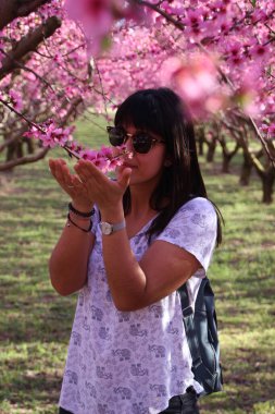 Beautiful woman smelling the pretty pink flowers of peach tree.