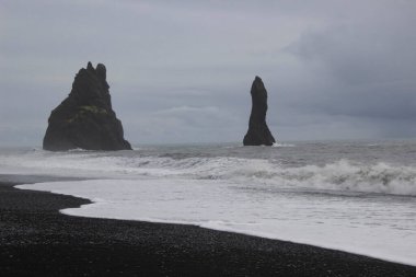 Reynisfjara 'nın kara kumsalı ve İzlanda' nın güney kıyısındaki Dyrholaey 'den Reynisfjall Dağı.
