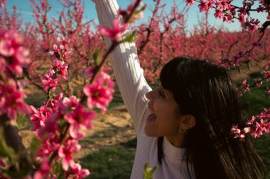 Baharda çiçek açan şeftali ağaçlarının arasında gülümseyen bir kadın.