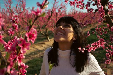 Baharda çiçek açan şeftali ağaçlarının arasında gülümseyen bir kadın.