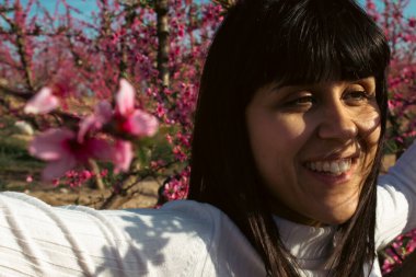 Baharda çiçek açan şeftali ağaçlarının arasında gülümseyen bir kadın.