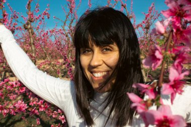 Baharda çiçek açan şeftali ağaçlarının arasında gülümseyen bir kadın.