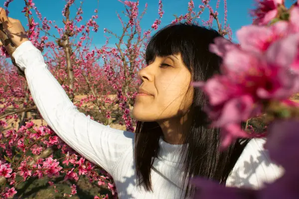 Beautiful woman smelling the pretty pink flowers of peach tree.