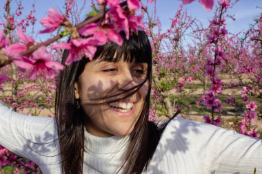 Baharda çiçek açan şeftali ağaçlarının arasında gülümseyen bir kadın.