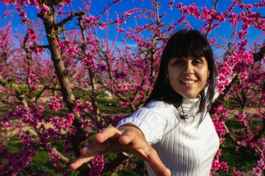 Güzel bir bahar öğleden sonrasında, çiçek açmış şeftali ağaçlarıyla el sıkışan bir kadın.