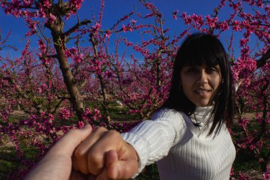 Güzel bir bahar öğleden sonrasında, çiçek açmış şeftali ağaçlarıyla el sıkışan bir kadın.