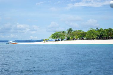 Sahilde bir cennet adasında tatil köyünün yanında, arka planda palmiye ağaçları ve botlar var..