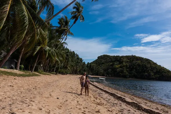Filipinler 'in tropik adasında gün batımında cennet kumsalının keyfini çıkaran güzel bir çift. Palmiye ağaçlarıyla çevrili..