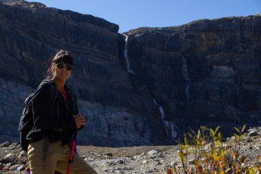 Sonbaharda güzel Kanada kayalıklarında yürüyen bir kadın yürüyüşçü güzel güneşli bir günde arka planda bir şelaleyle