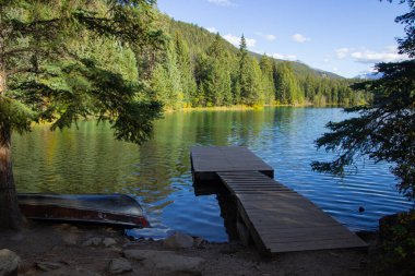Güneşli bir günde, Beş Göller Vadisi, Jasper Ulusal Parkı, Alberta, Kanada 'da ormanlık ve dağ manzaralı sakin bir göl üzerindeki ahşap rıhtım.