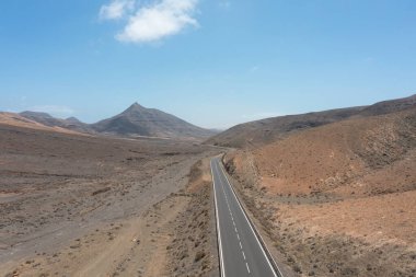 Fuerteventura, Kanarya Adaları 'ndaki Sicasumbre Dağı yakınlarındaki kurak volkanik araziden geçen uzun ve düz bir yolun insansız hava aracı görüntüsü.. 