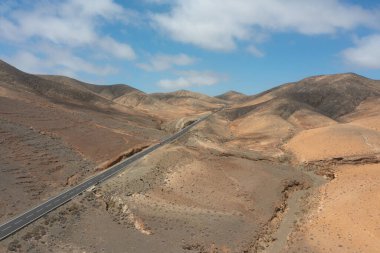 Fuerteventura, Kanarya Adaları 'ndaki Sicasumbre Dağı yakınlarındaki kurak volkanik araziden geçen uzun ve düz bir yolun insansız hava aracı görüntüsü.. 