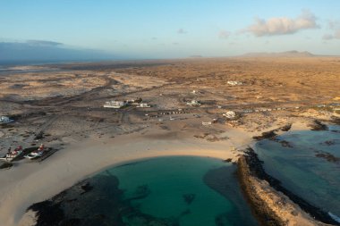 Fuerteventura 'daki Playa Chica' nın nefes kesici hava manzarası, kristal berrak turkuaz sular, yumuşak altın kum ve volkanik kaya oluşumları. 