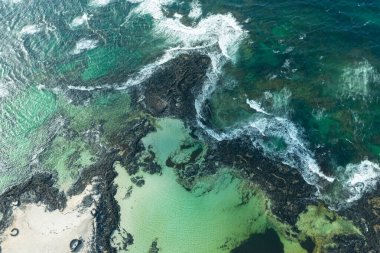 Los Charcos Plajı 'nda kumların üzerine inşa edilmiş eşsiz taş kaplamaları gösteren Idyllic deniz manzarası.