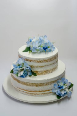 Beyaz arka planda mavi çiçeklerle süslenmiş vejetaryen çıplak düğün pastası.