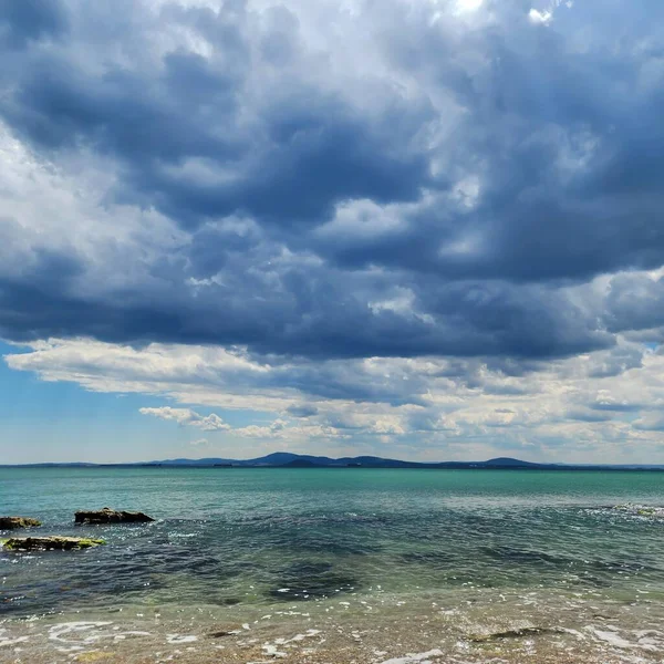 Turkuaz denizin taştan sığ suları. Mavi deniz ufkunda fırtına bulutları.