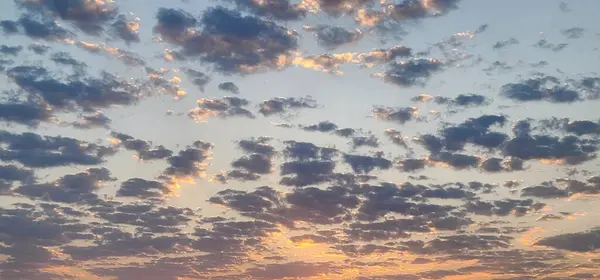 Kümülüs bulutlarıyla kaplı büyüleyici bir akşam göğü. Gün batımında şeftali gökyüzü