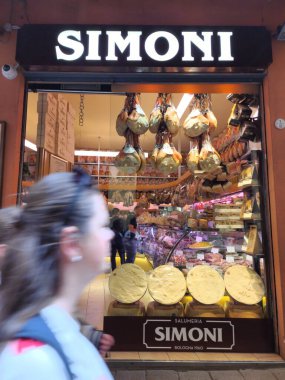 Bir İtalyan marketinin renkli vitrinleri. Bir kadın dükkan penceresinin önünden hızla geçer.