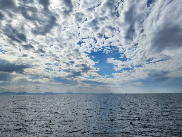 Kümülüs bulutlarının deniz ufkunda mavi gökyüzündeki güzelliği. Deniz yüzeyinde şamandıralar