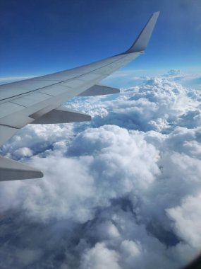 Parlak mavi gökyüzünün altında dönen bulutların üzerinde uçan bir uçağın kanadı.