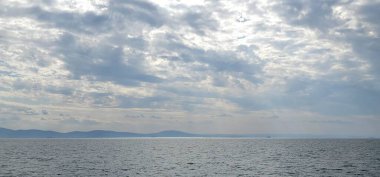 Akşam manzarasında deniz ufkunun üzerinde parlayan bulutlar.