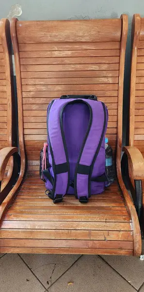 Eski bir tren istasyonunun ahşap sandalyesinde mor bir gezginin sırt çantası.