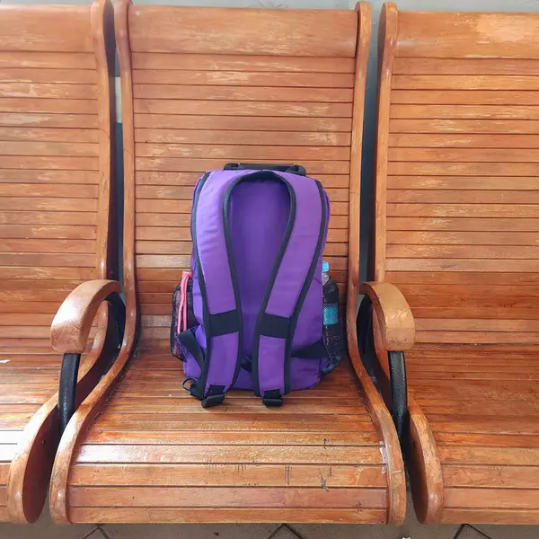 Eski bir tren istasyonunun ahşap sandalyesinde mor bir gezginin sırt çantası.