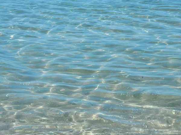 Kumlu sığ denizde mavi su. Güneş su yüzeyinde parıldıyor.