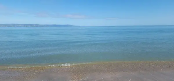 Rahatlatıcı mavi deniz manzarası. Sakin deniz kumlu sahilde yavaşça dalgalanır.