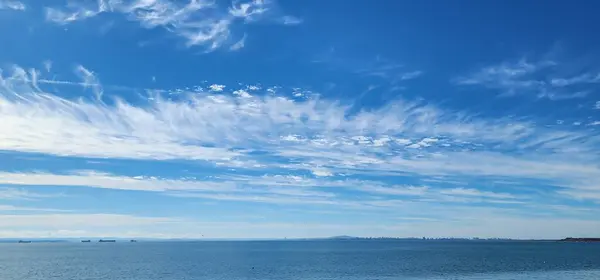 Mavi gökyüzünde geniş bir sirrus bulutu şeridi. Rüzgâr, denizin üzerinde bulutları dağıtır.