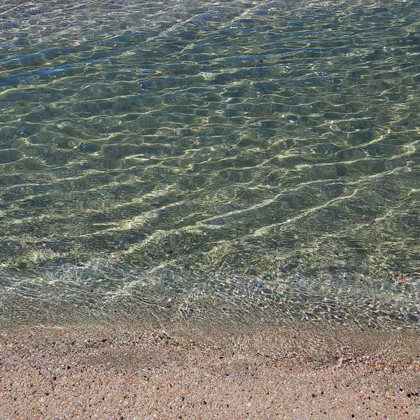 Güneş kumlu sahilin yakınındaki deniz suyunda dalgalanır