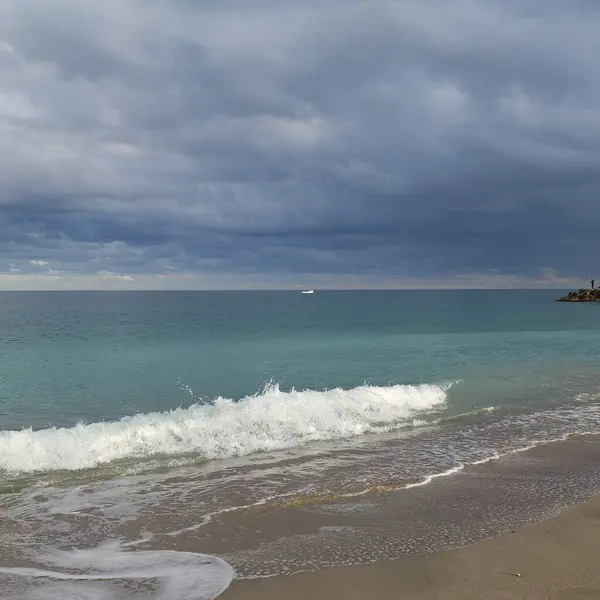 Turkuaz bir deniz köpüklü dalgası kumlu kıyıya doğru ilerliyor.